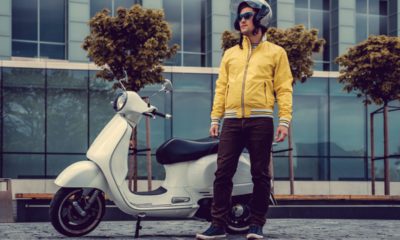 A man in yellow jacket and sunglasses posing near white scooter.